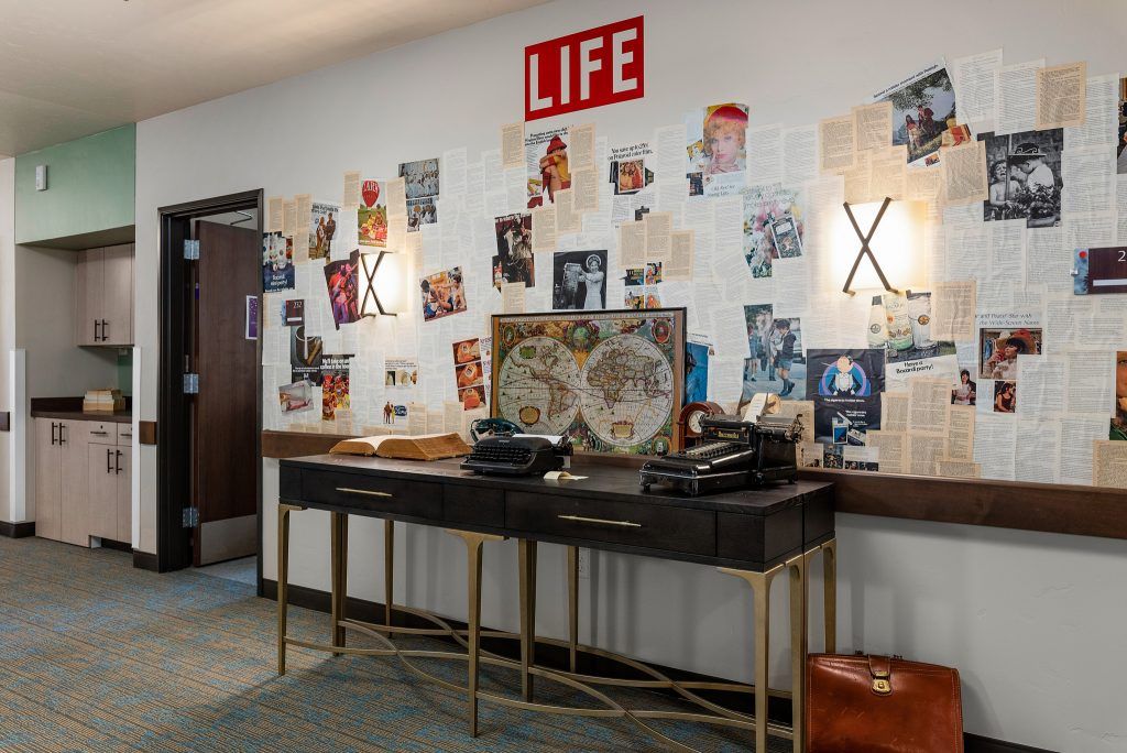 A retro office setup featuring a desk with typewriters and a wall decorated with magazine cutouts.