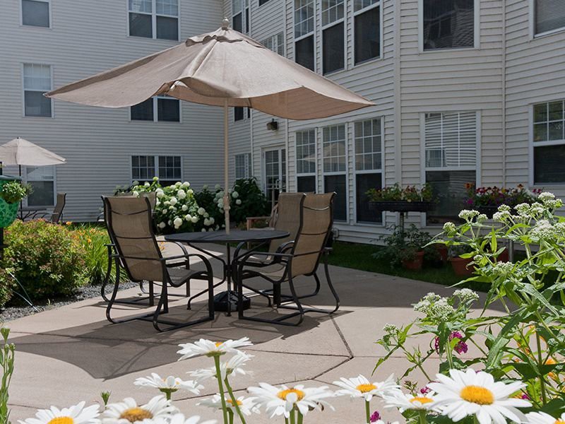 A cozy patio setup with chairs and an umbrella surrounded by blooming flowers beside a building.