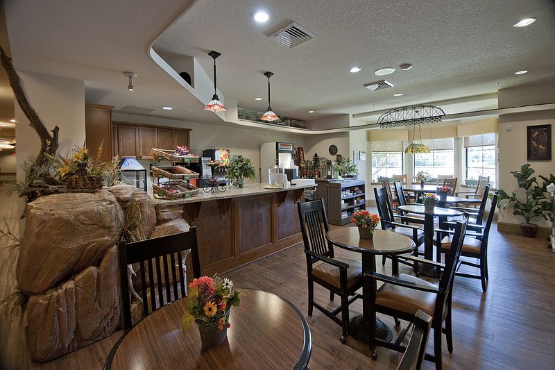 A cozy cafe interior with neatly arranged tables and chairs, a service counter, warm lighting, and decorative elements.
