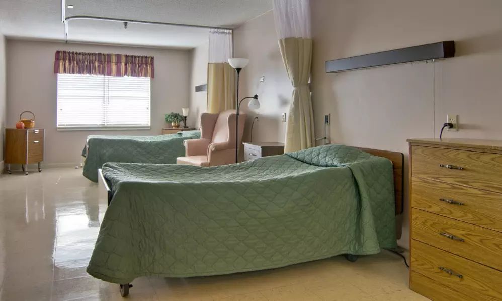A hospital room with two neatly made beds, separated by privacy curtains.