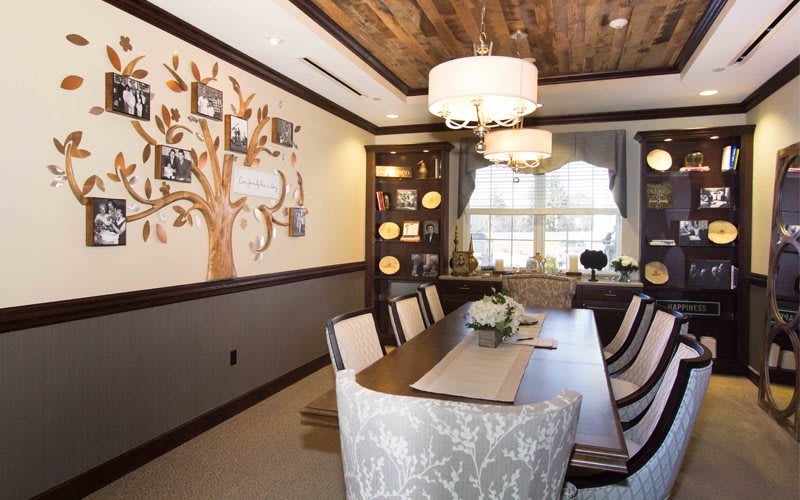 A beautifully designed dining room featuring a wooden ceiling, elegant chandeliers, and a wall adorned with family photo tree art.