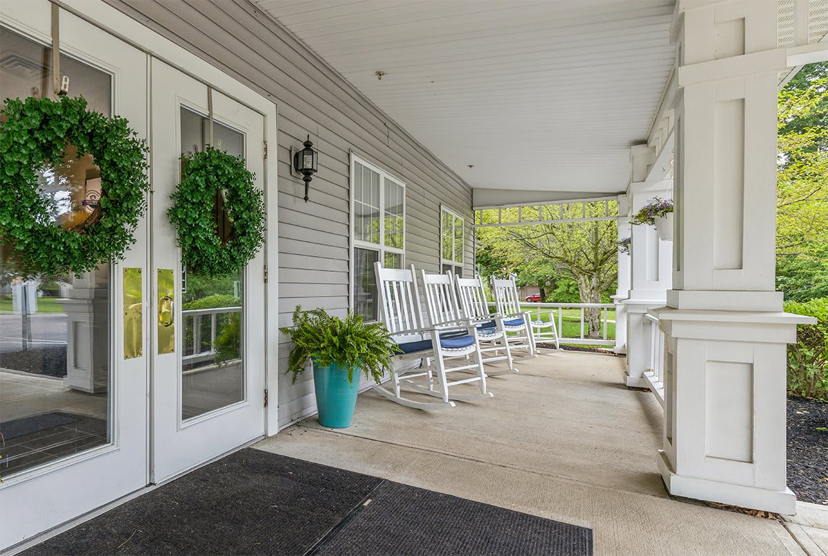 A cozy porch with white rocking chairs and a welcoming front door adorned with a green wreath.