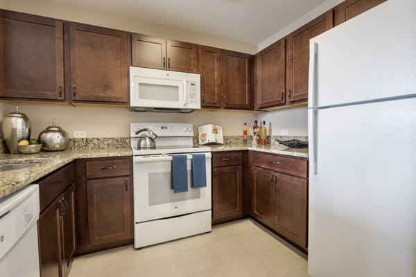 A modern kitchen with wooden cabinets, white appliances including a microwave, oven, and refrigerator.