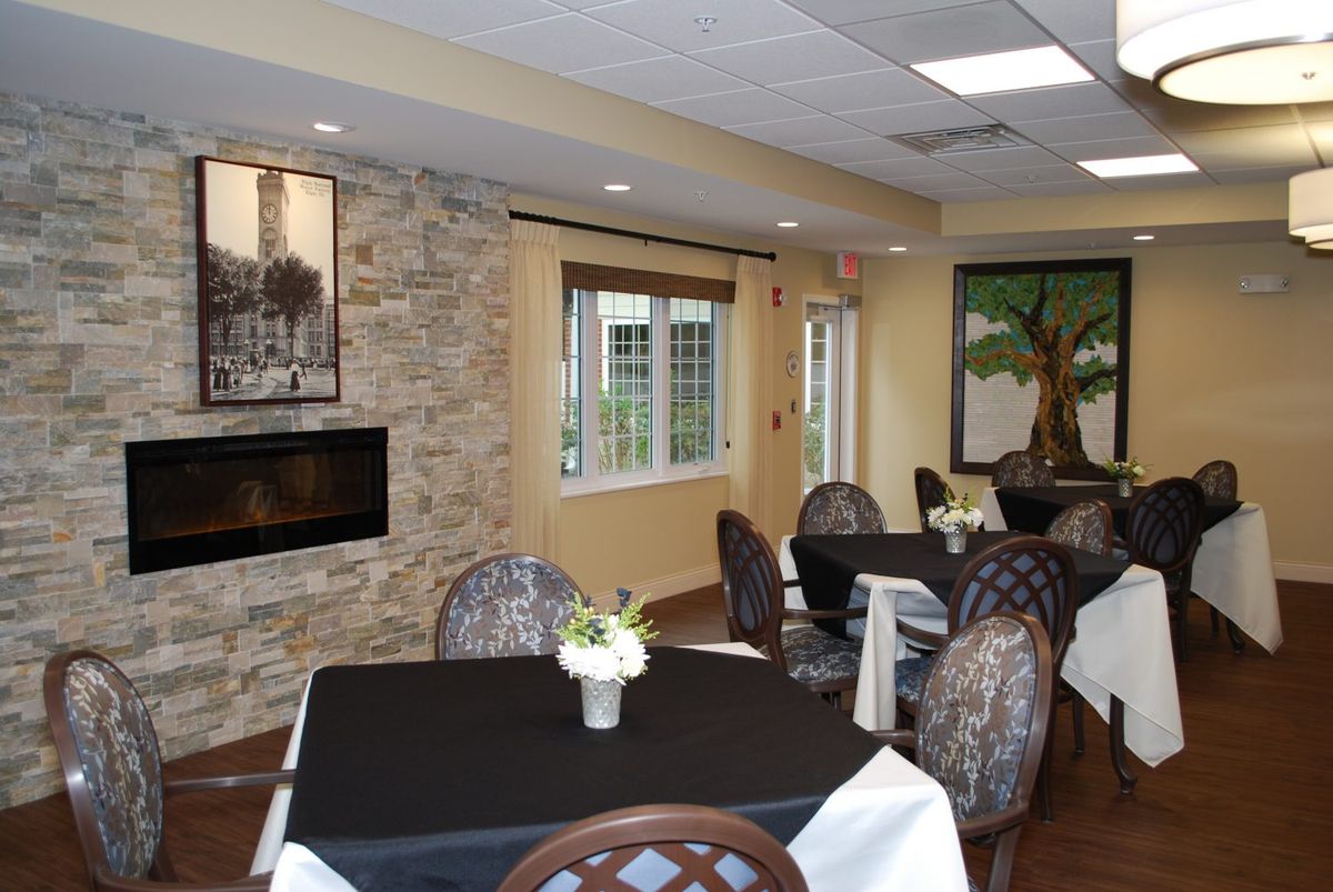 A cozy dining room with neatly arranged tables and chairs, featuring a fireplace and decorative artwork on the walls.