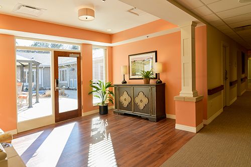 A warmly lit lobby entrance with wooden flooring, a decorative cabinet, and indoor plants.