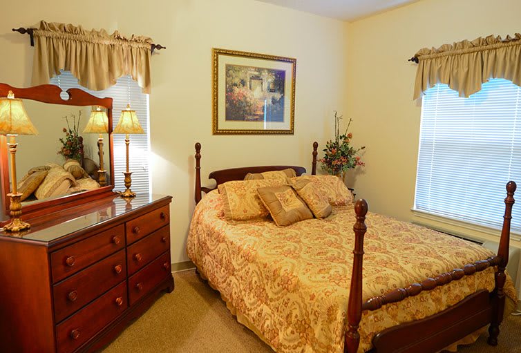 A cozy bedroom featuring a classic wooden bed and matching dresser, with warm lighting and elegant decor.