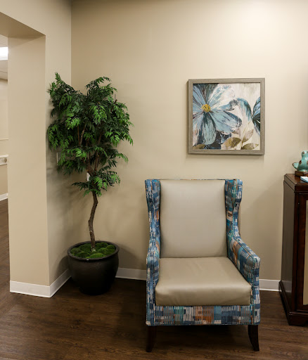 A cozy corner featuring a patterned chair, a decorative plant, and artwork on the wall.