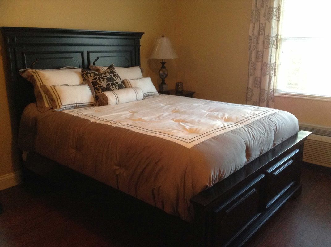 A cozy bedroom with a neatly made bed and decorative pillows, featuring a bedside lamp and elegant curtains.