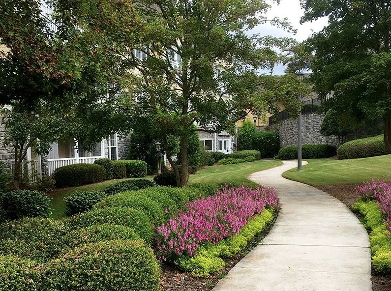 A scenic pathway lined with vibrant flowers and lush greenery in a residential neighborhood.