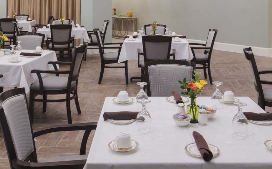 A neatly arranged dining area with tables set for guests, featuring floral centerpieces.