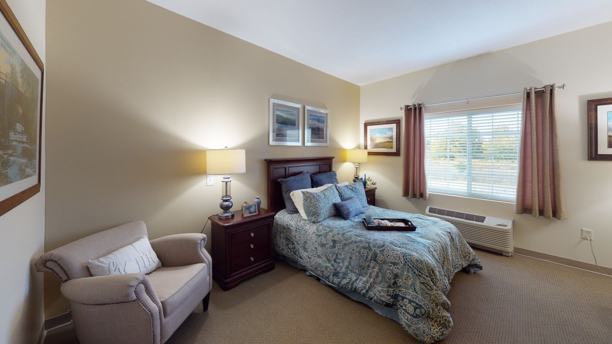 A cozy bedroom with a bed, two lamps, and a comfortable chair by the window.
