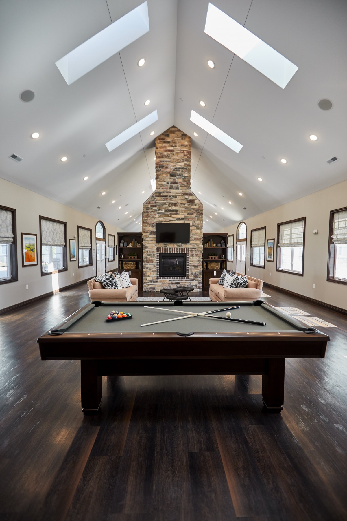 A luxurious game room featuring a pool table, stone fireplace, and high ceilings with skylights.