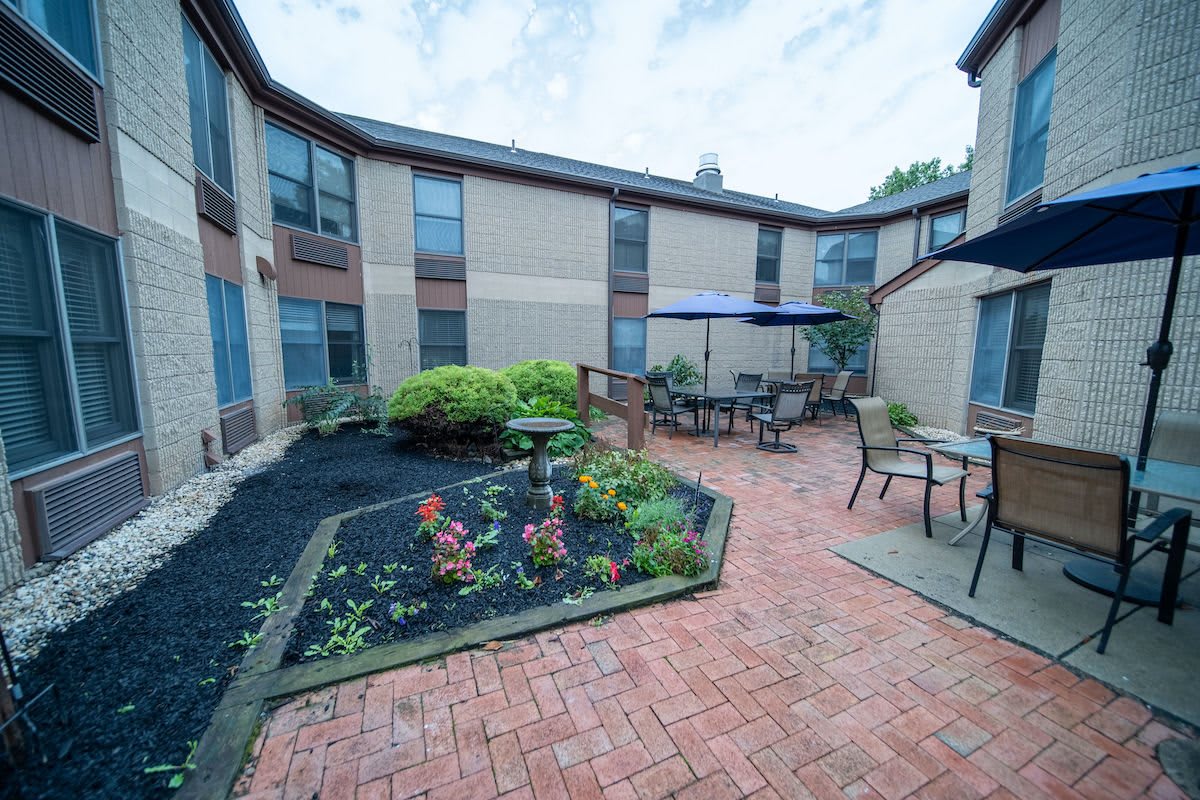A serene courtyard featuring a brick pathway, garden beds, and outdoor seating with umbrellas.