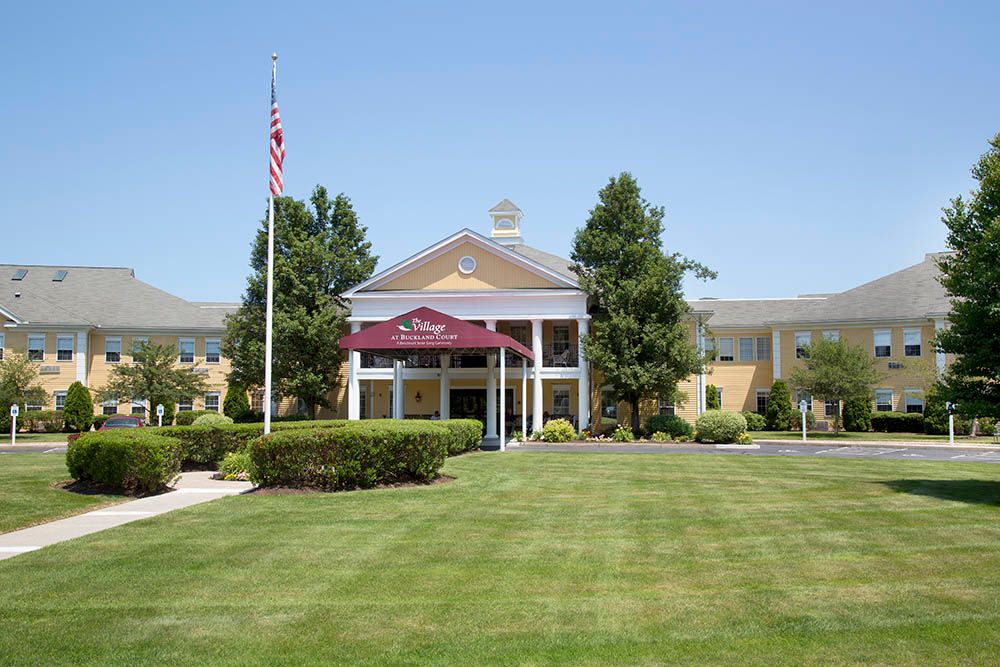 The entrance of a hotel with a landscaped lawn and flagpole.