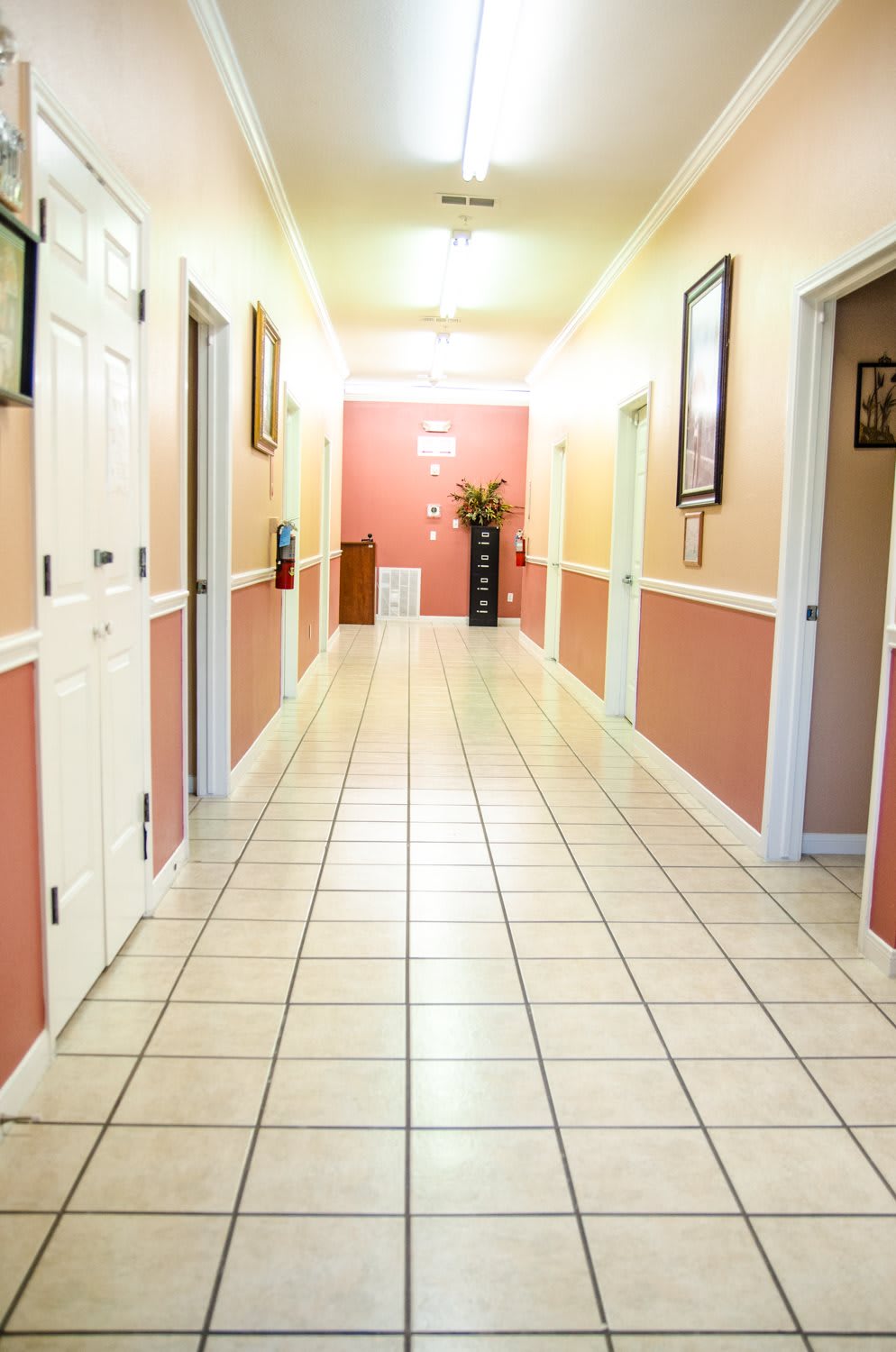 A well-lit hallway with tiled flooring and multiple doors leading to rooms.
