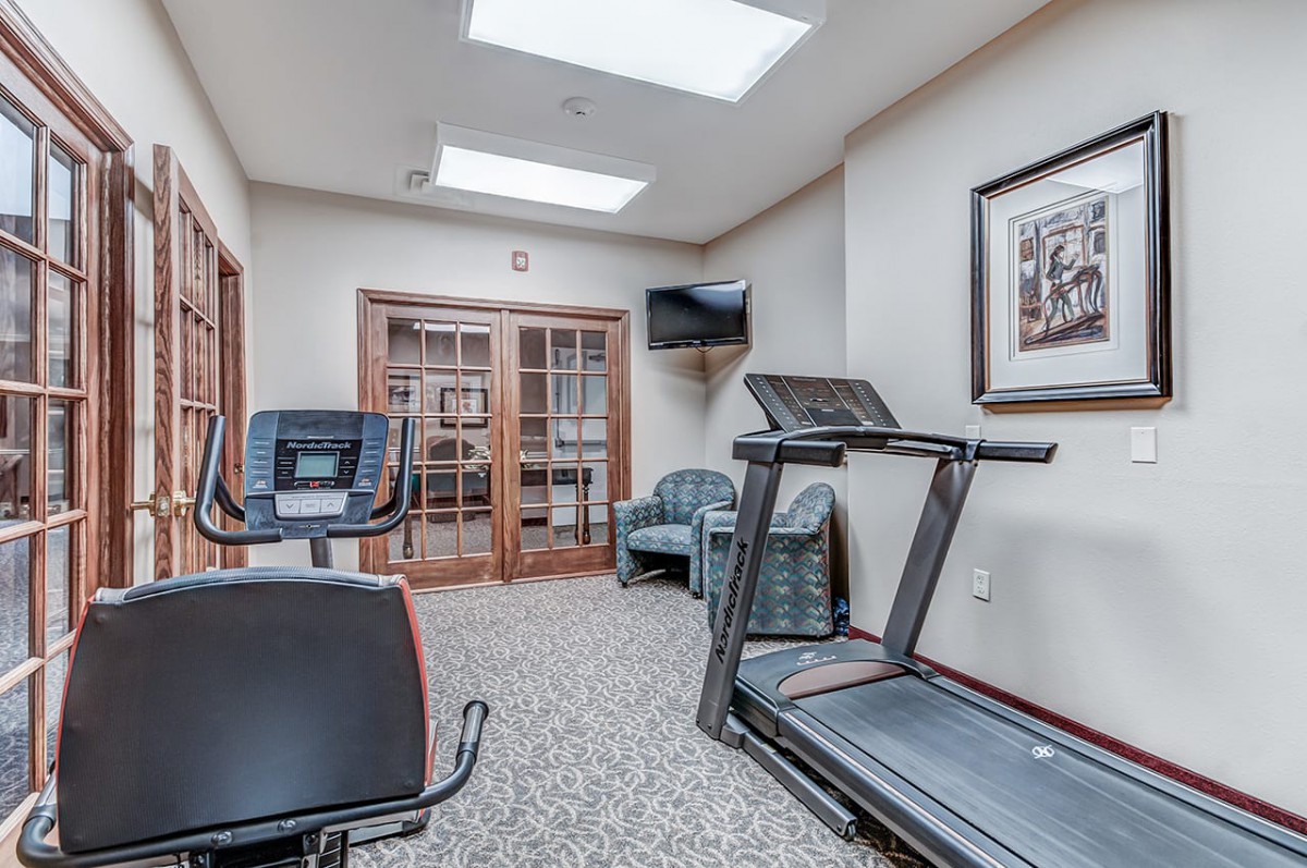 A small fitness room equipped with a treadmill, stationary bike, and a wall-mounted television.