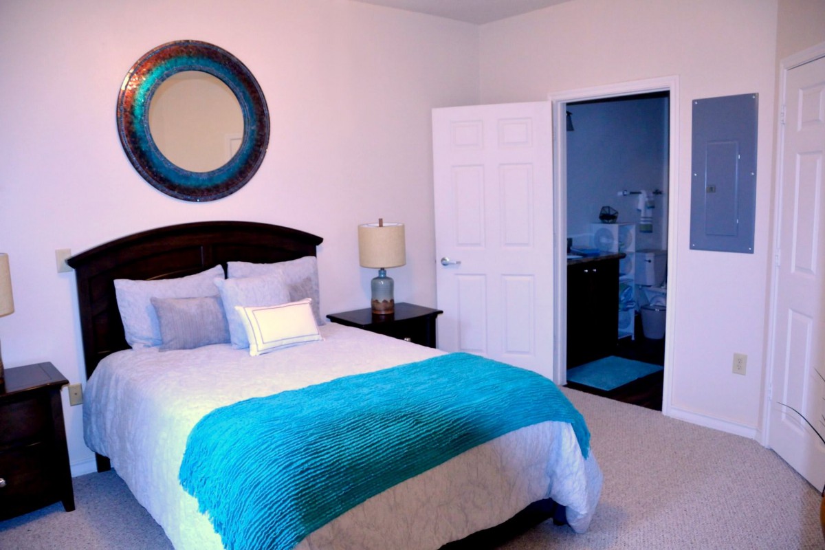 A cozy bedroom with a bed, decorative mirror, and a lamp by the nightstand.