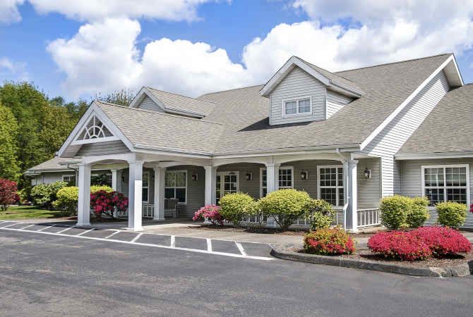 A charming white building with a landscaped garden and colorful flowers under a bright blue sky with clouds.