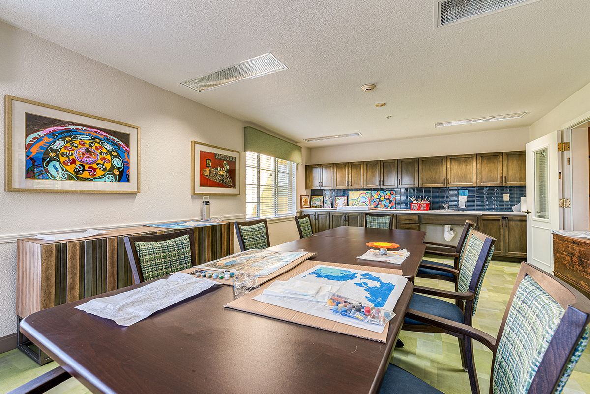 A spacious conference room with a long table, chairs, vibrant artwork on the walls, and a kitchenette in the background.