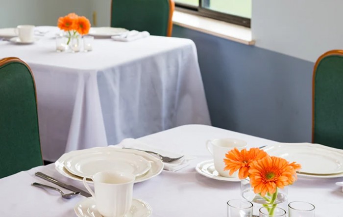 A neatly set dining table with white tablecloths and orange flowers as decoration.