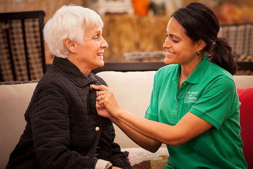 A caregiver assists an elderly woman with her clothing, showcasing compassion and support.