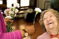 An elderly woman joyfully receives flowers from a caregiver.