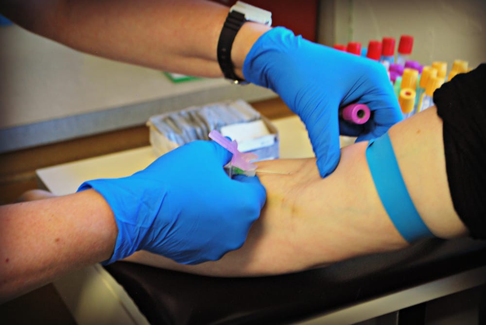 A healthcare professional performs a blood draw on a patient using protective gloves.