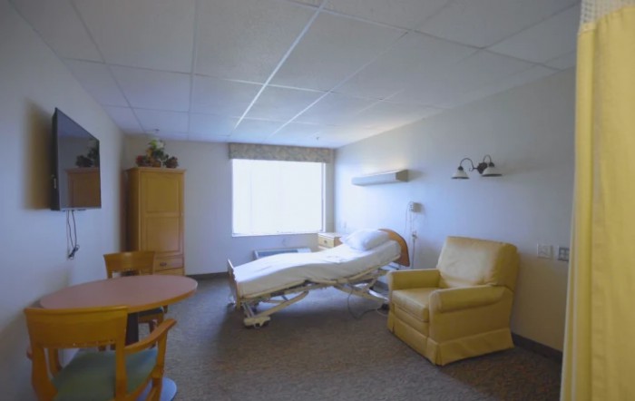 A clean hospital room with essential furniture including a bed, chair, and window.