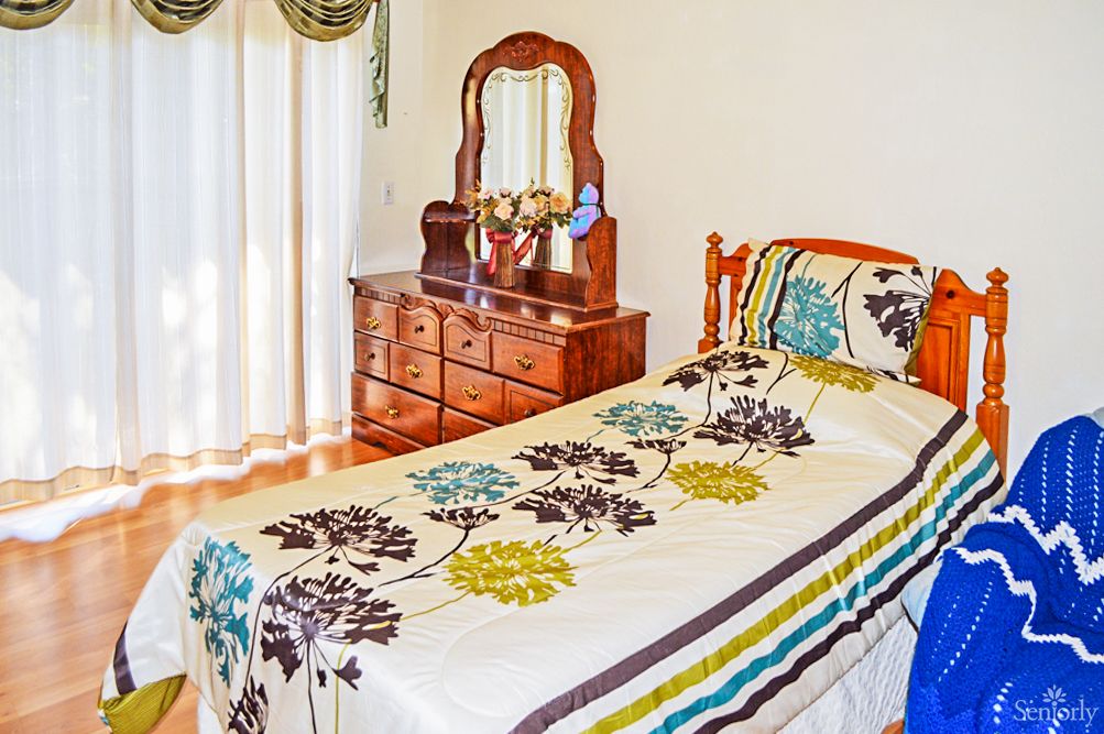 A cozy bedroom with a single bed featuring floral bedding, alongside a wooden dresser and mirror.