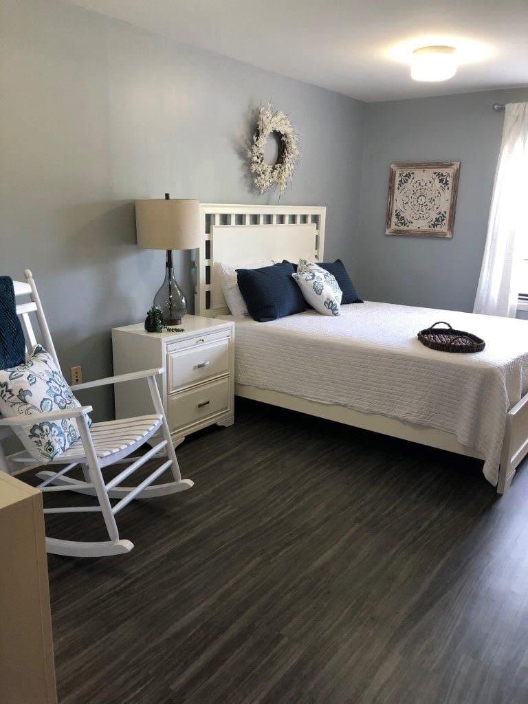 A cozy bedroom with modern decor featuring a bed, nightstand, lamp, and rocking chair.