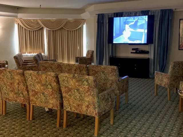 A cozy theater room with rows of floral-patterned chairs facing a large screen.