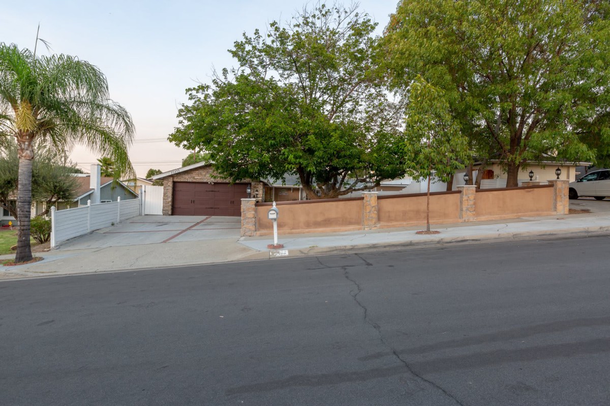 A suburban house with a driveway, garage, and trees enclosed by a brick fence.