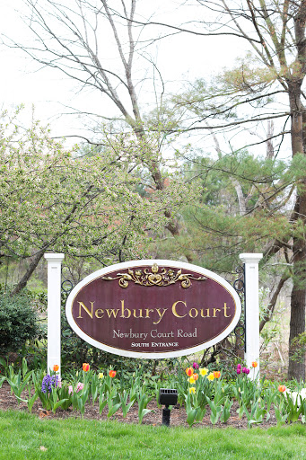 Welcome sign for Newbury Court, surrounded by blooming nature.