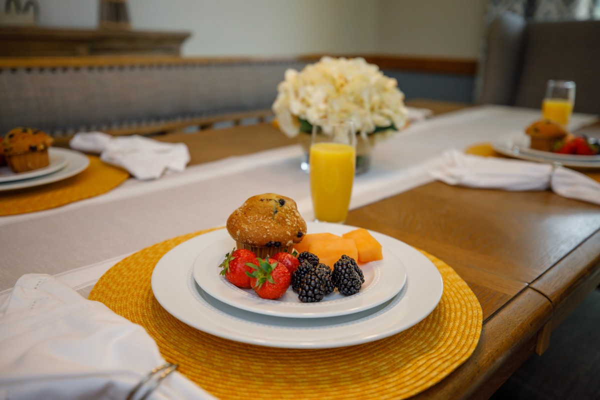 A breakfast setting featuring a muffin, fresh berries, and orange juice on a neatly arranged table.