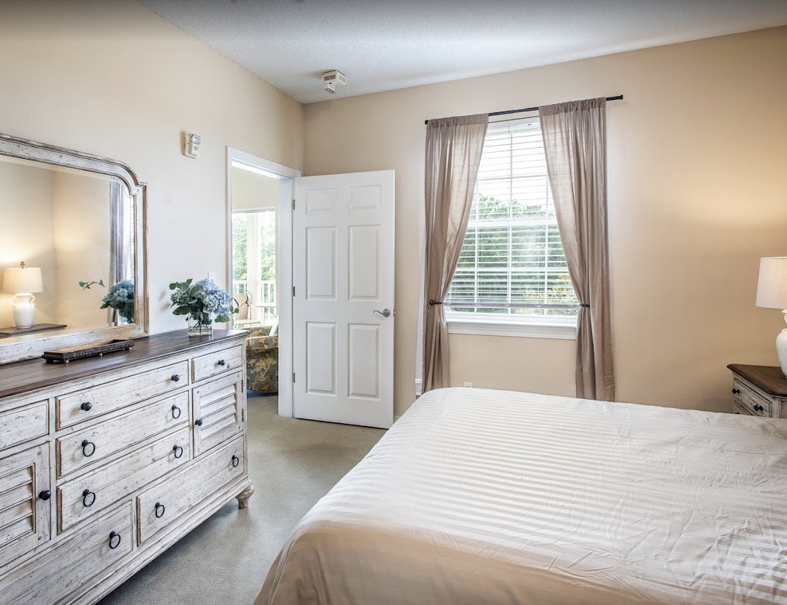 A cozy bedroom with a bed, dresser, and window with curtains.