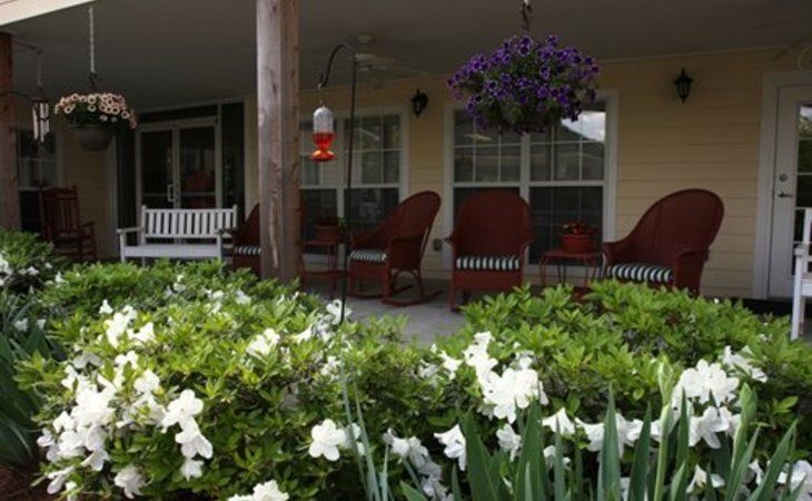 A cozy porch with comfortable seating overlooks a garden filled with blooming flowers.