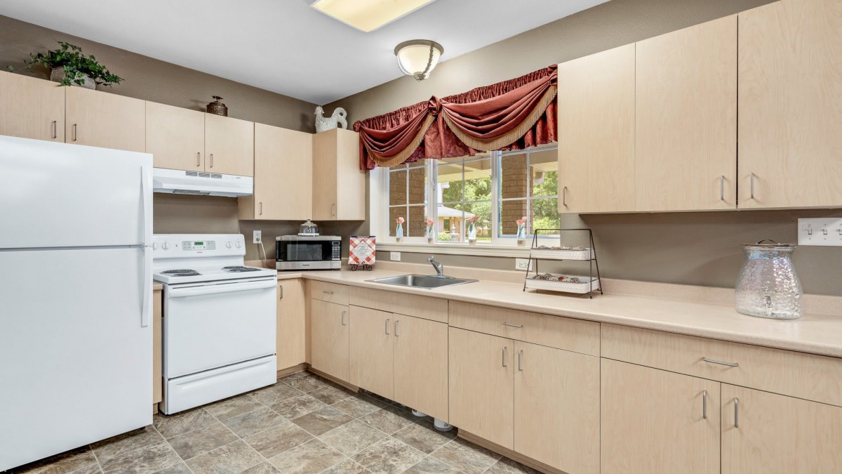 A cozy kitchen with light wood cabinets, a stove, and a microwave, featuring a window adorned with red curtains.