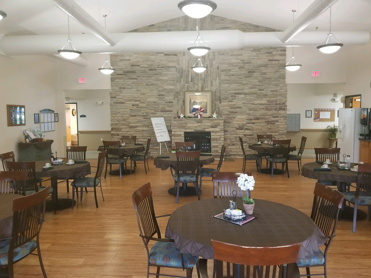 A cozy dining area with round tables, chairs, and a stone fireplace.