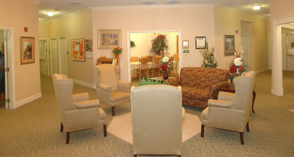 A cozy living room with a seating area featuring chairs and a sofa, decorated with plants and artwork.
