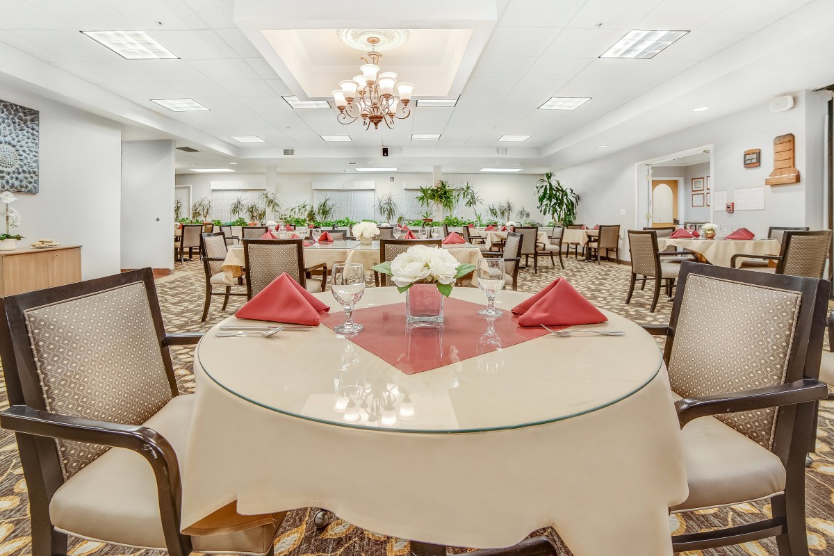 An elegant dining room with neatly set tables and a chandelier hanging from the ceiling.