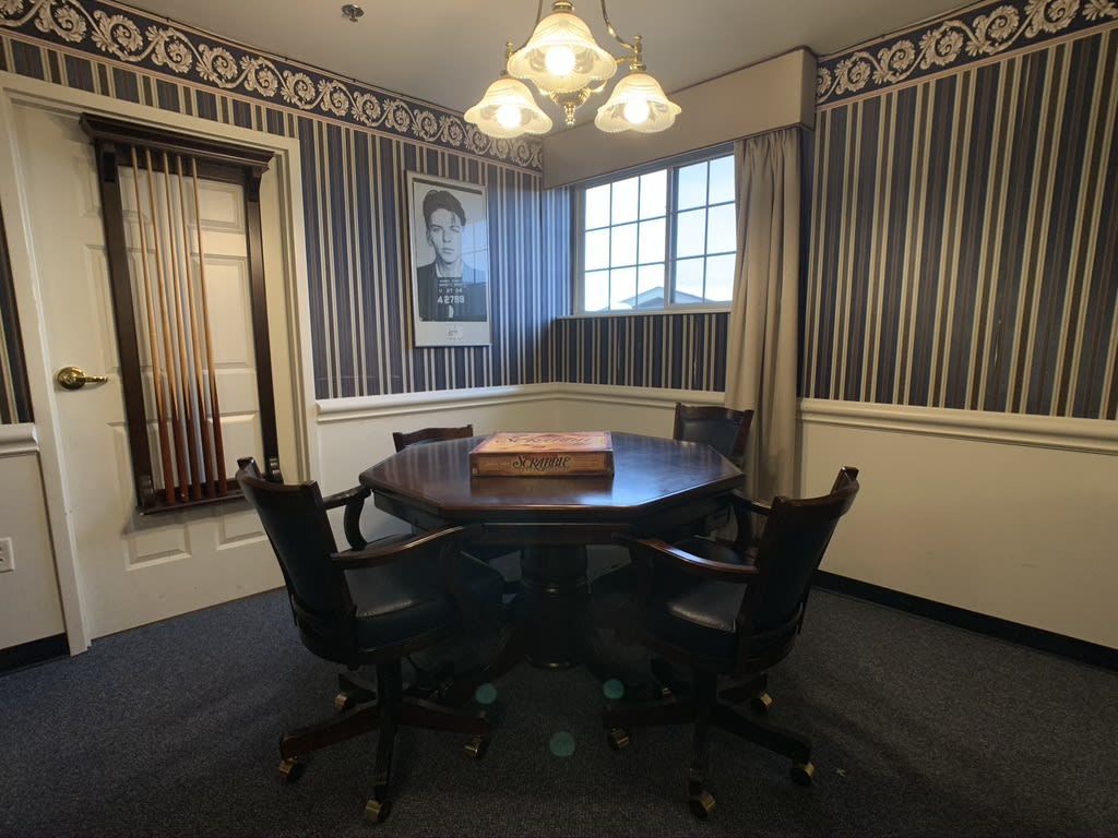 A classic meeting room with a round table, surrounded by chairs and adorned with striped wallpaper and a portrait.