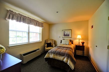 A cozy bedroom with a single bed, chair, and warm lighting.