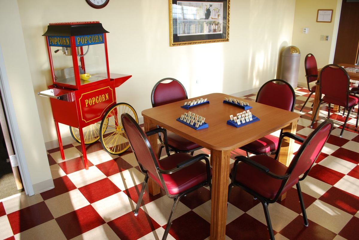 A cozy game room featuring a table with bingo cards, surrounded by chairs and a vintage popcorn machine on a checkered floor.