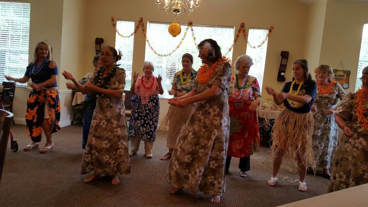 A group of elderly individuals participating in a Hawaiian-themed dance indoors.