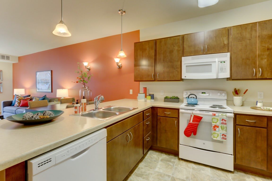 A cozy kitchen interior with wooden cabinets, a white oven and microwave, and a double sink.