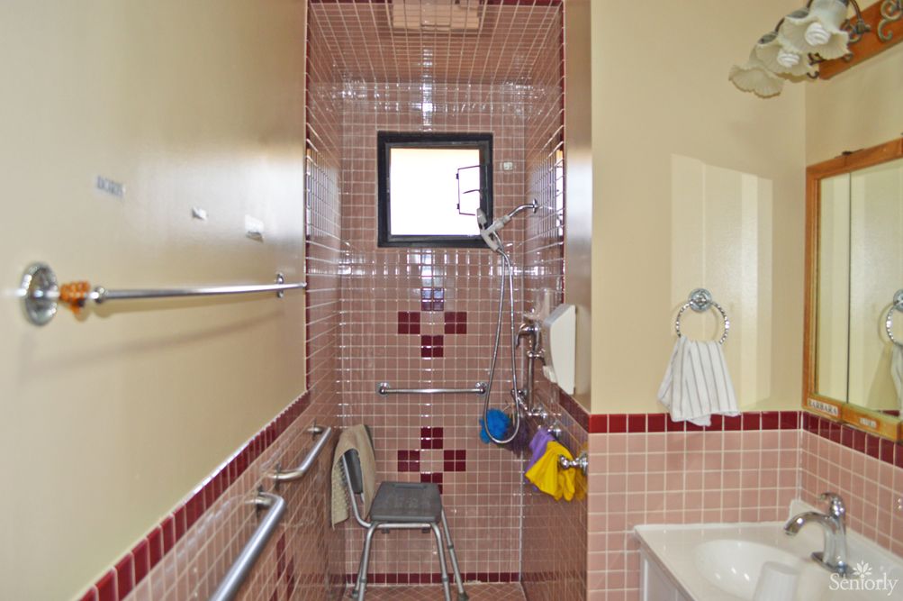 A bathroom with red tiled shower area equipped with a shower chair and grab bars.