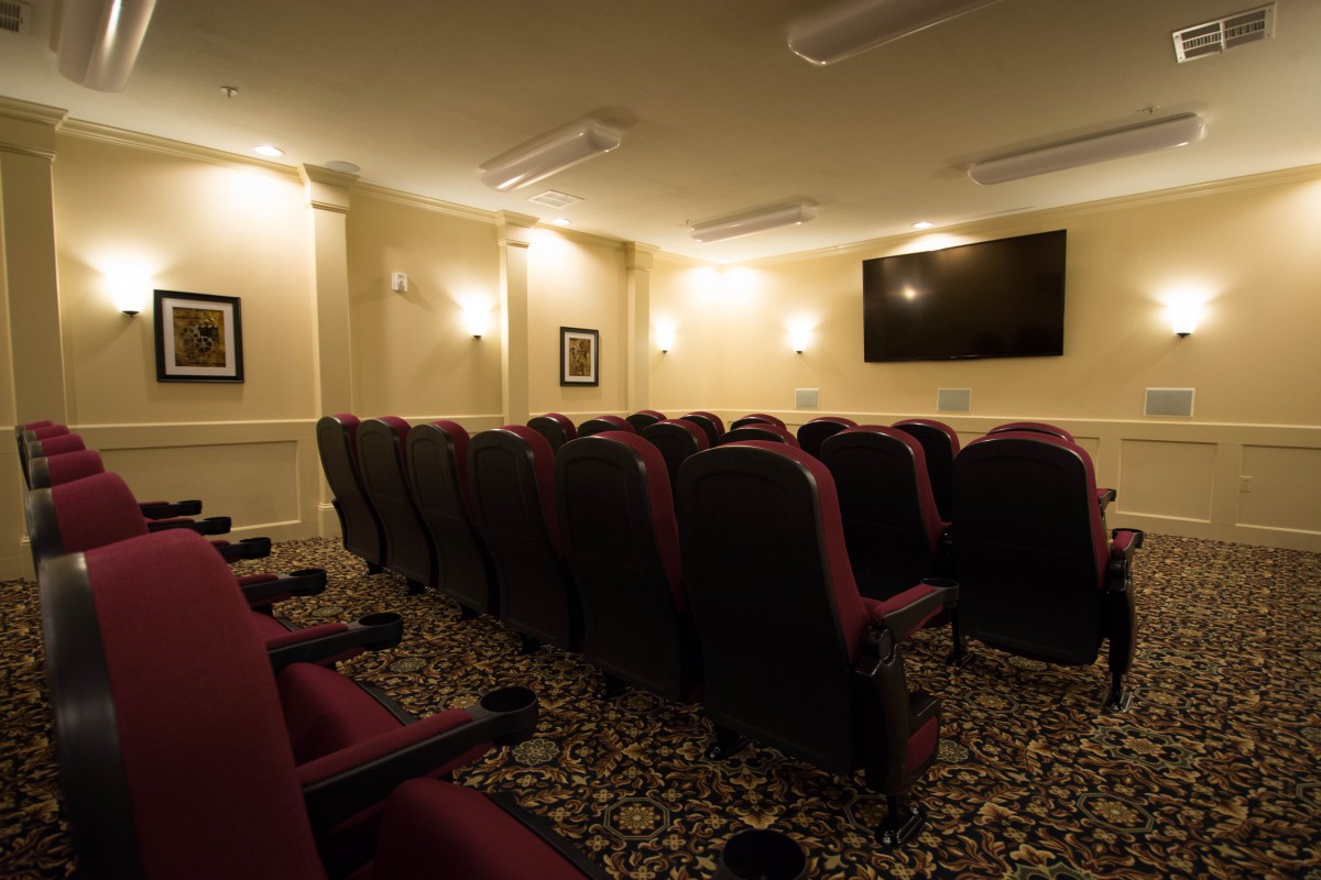 An indoor theater room with rows of comfortable seating and a large screen on the wall.