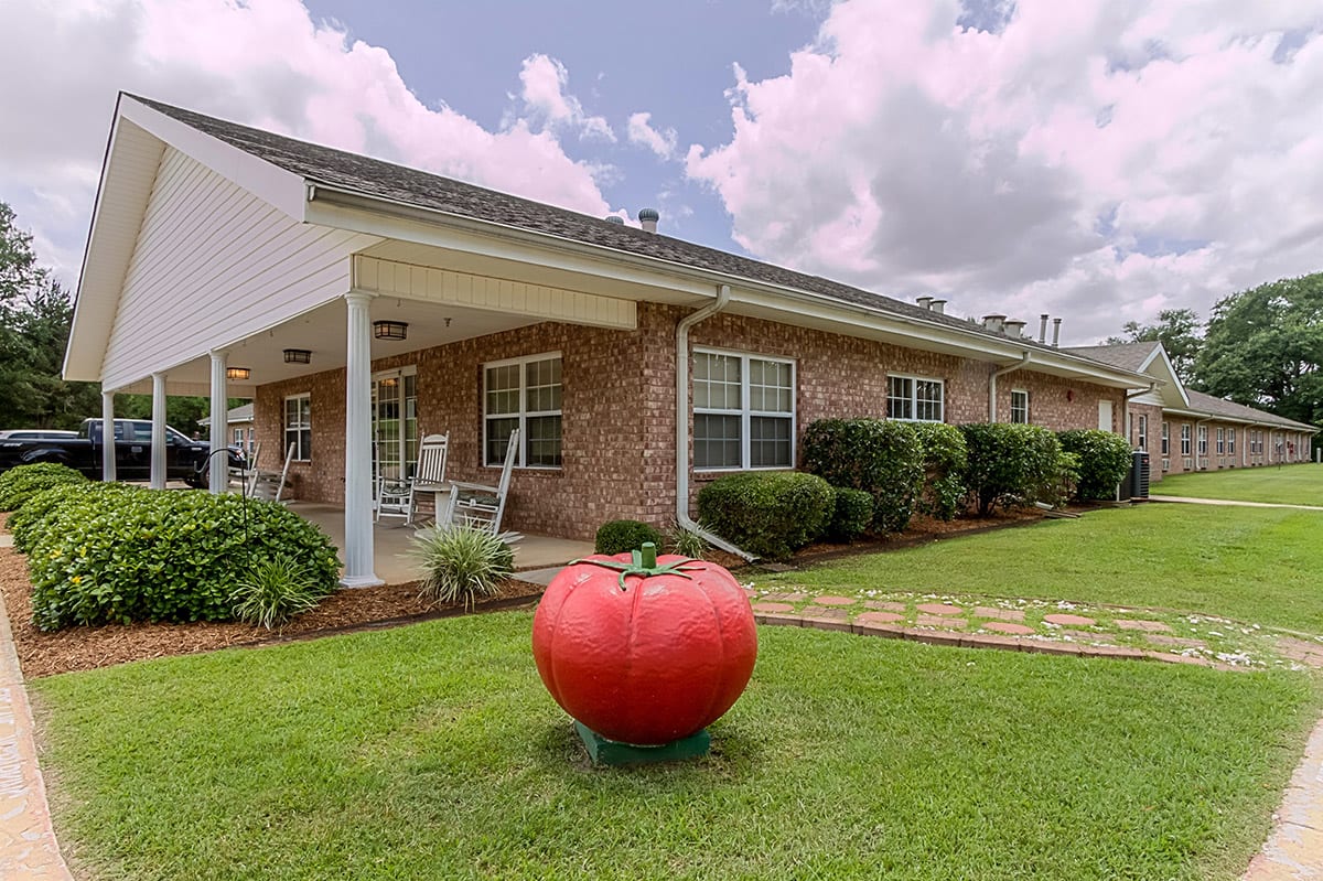 A large tomato sculpture on a well-maintained lawn in front of a house.