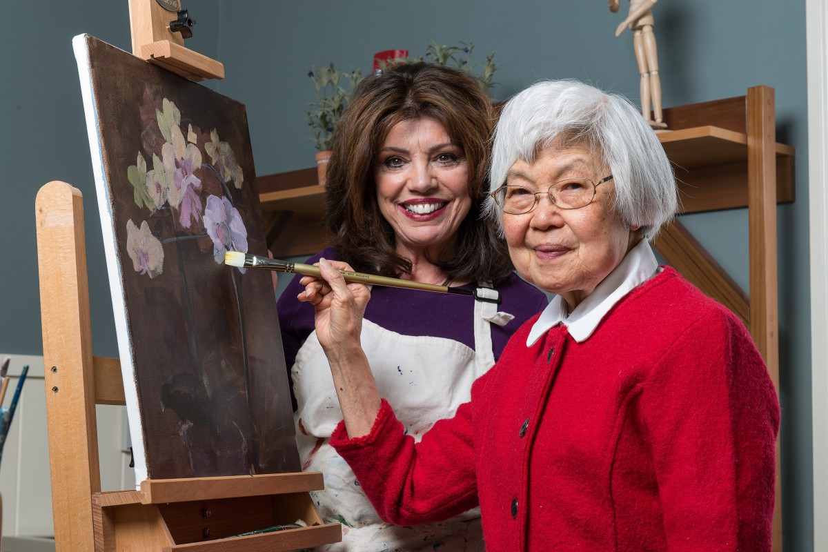 Two women enjoying a painting session together, with one of them holding a paintbrush in front of a canvas.