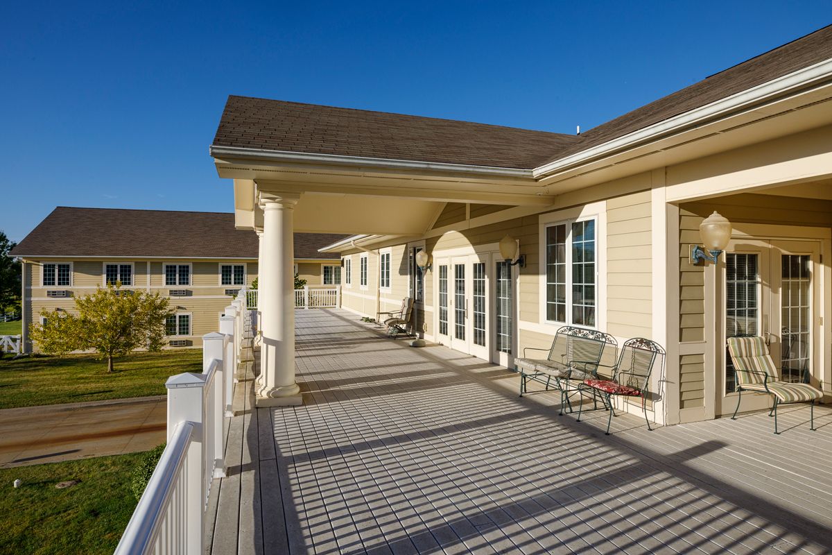 A spacious veranda with chairs, part of a modern building under a clear blue sky.